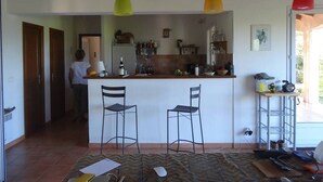 Cuina amb dos tamborets de bar, un taulell ple d'objectes diversos i llums penjants.