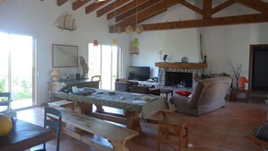 Un saló rústic amb bigues de fusta a la vista, una llar de foc, una televisió i una zona de menjador amb taula i bancs de fusta.