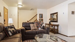 A living room with a brown leather sofa, a glass coffee table, and a plaid blanket on the sofa. - Outpost: Vine Street 2 - Close to Snow King! (Jackson)