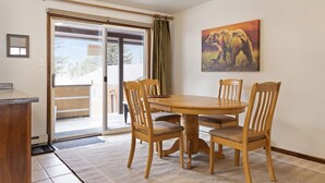A dining area with a wooden table and chairs, a painting on the wall, and a sliding glass door leading outside. - Outpost: Vine Street 2 - Close to Snow King! (Jackson)
