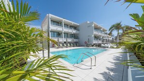 Un hôtel moderne doté d’une piscine, de chaises longues et de palmiers.