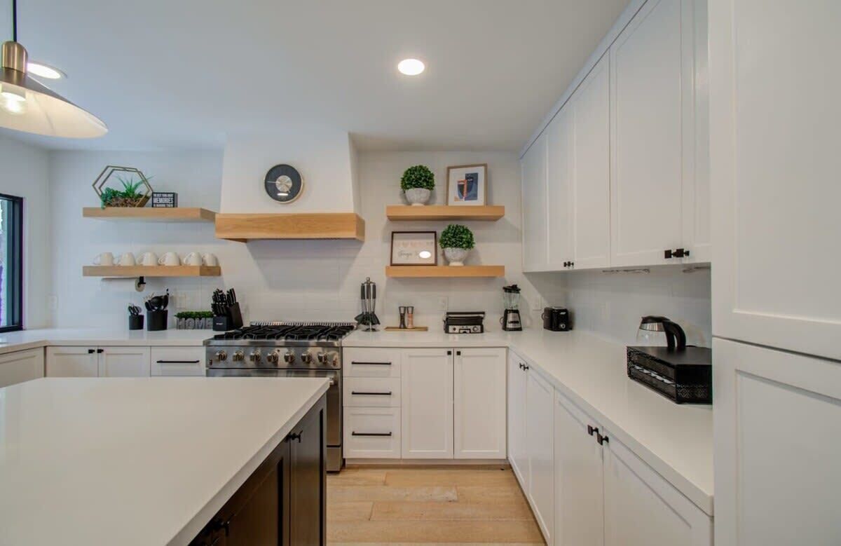 Una cocina moderna con armarios blancos, estantes de madera y una isla central.