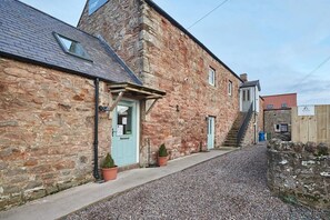 Traditional stone building with a sloped roof, featuring a single entrance with a door and potted plants.