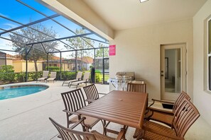 En overdækket terrasse med pool, udendørs møbler og grill.