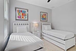 A bedroom with two beds, a nightstand, a lamp, and two abstract art pieces on the wall.
