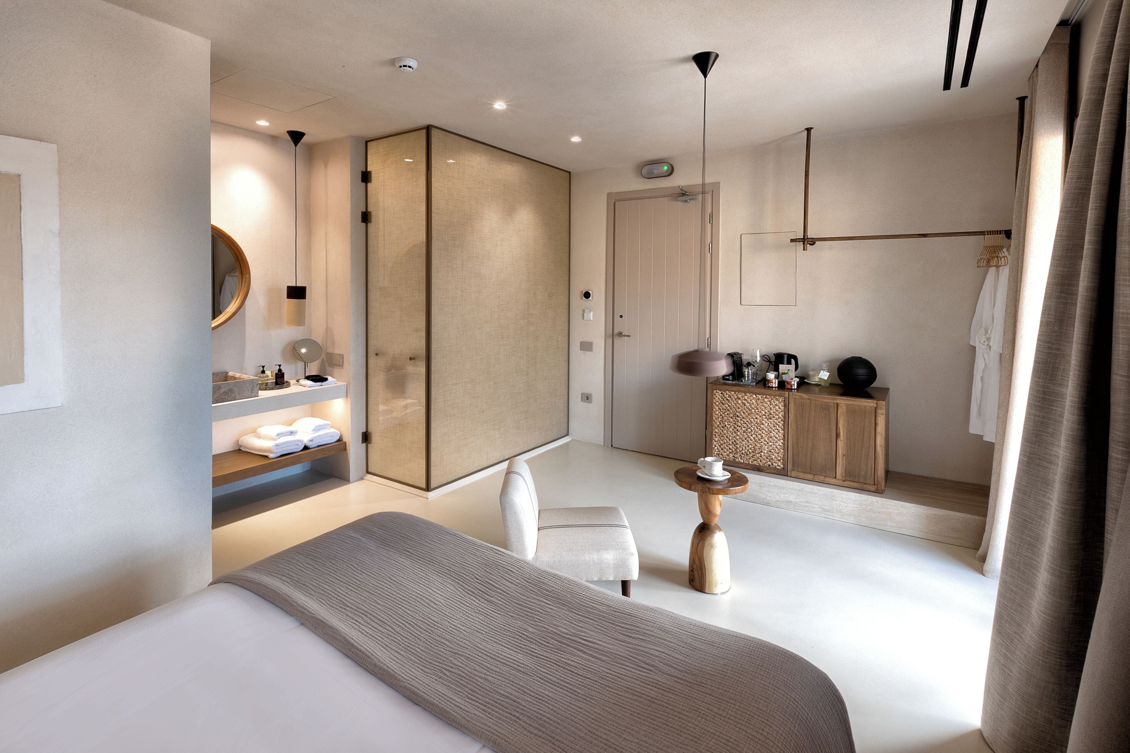 Una habitación de hotel moderna con una cama grande, un tocador con espejo, un pequeño rincón de descanso y un armario de madera.