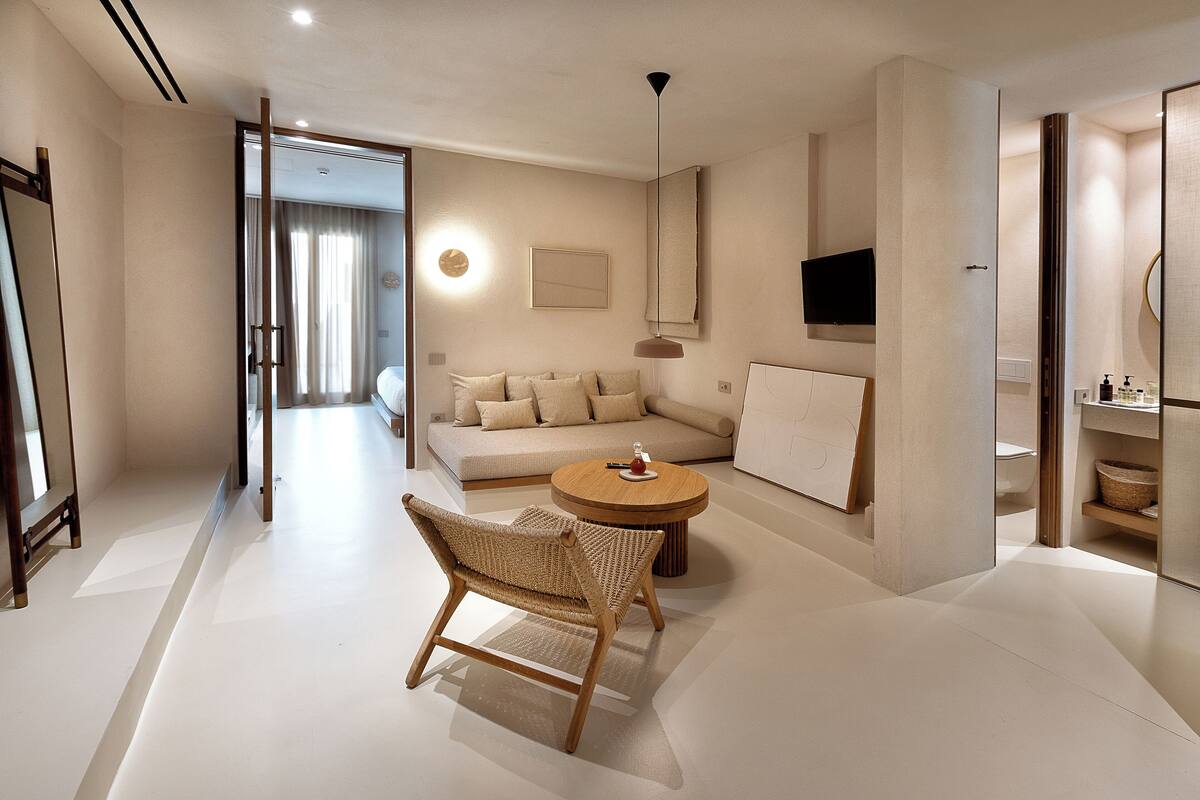 A modern hotel room with a sofa, a round table, and a wicker chair.