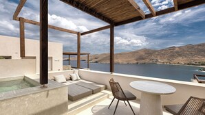 A terrace with a hot tub, seating, and a table with chairs, overlooking a body of water and hills.