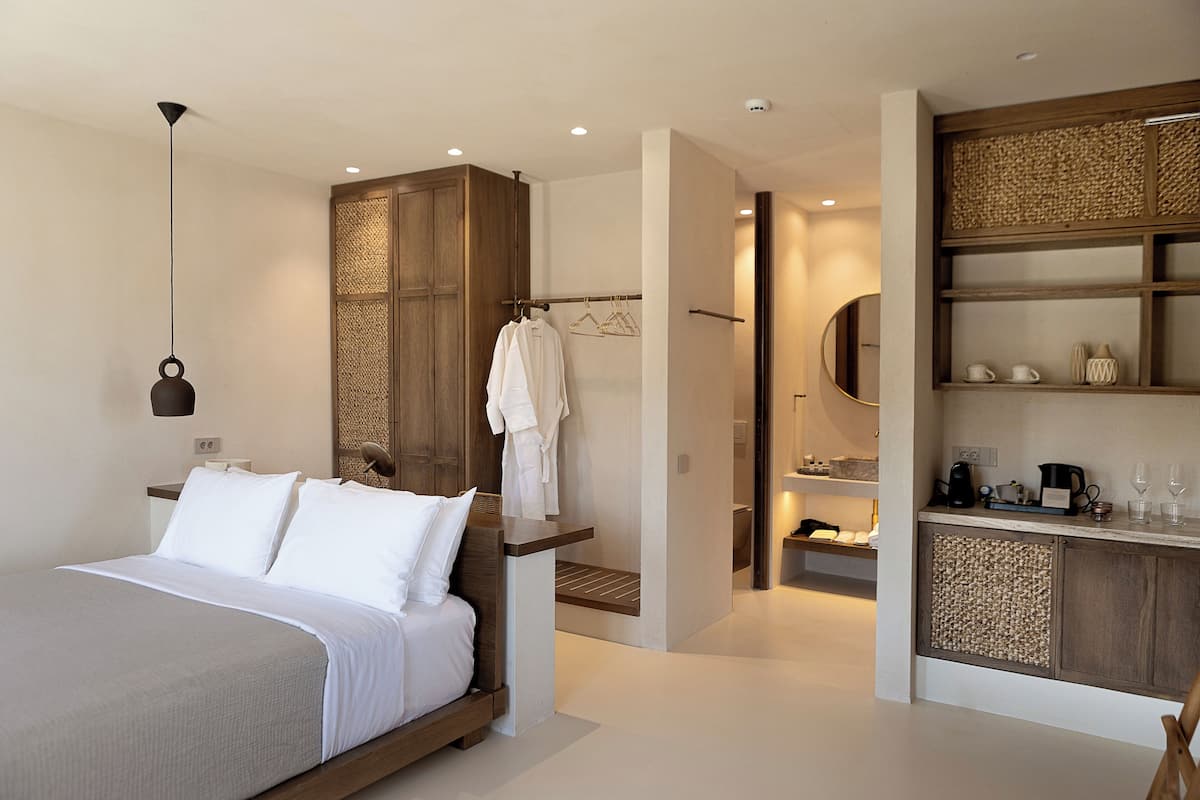A modern bedroom with a large bed, a wooden wardrobe, and a small kitchenette area.