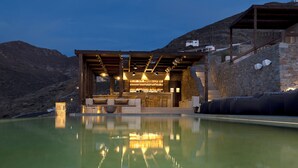 A poolside area with a bar and seating, surrounded by stone walls and a mountainous backdrop.