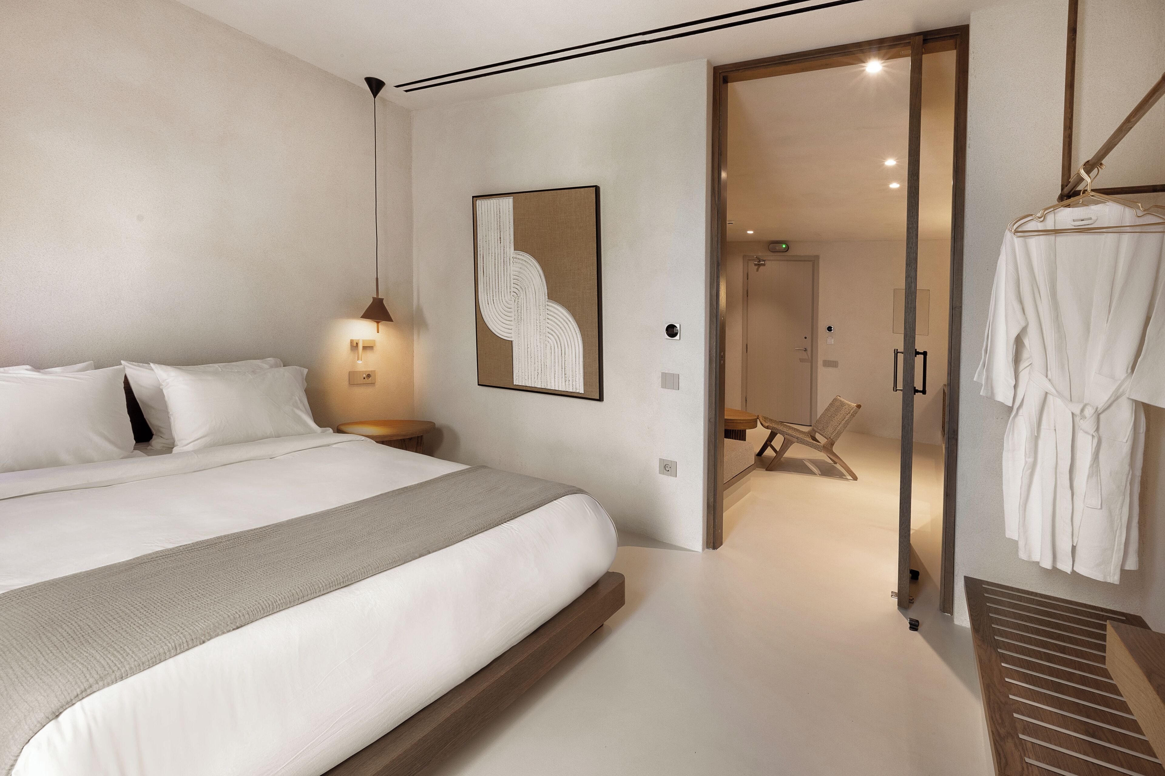 A modern bedroom with a large bed, a bedside table, a wall-mounted artwork, and a walk-in closet with hanging robes.