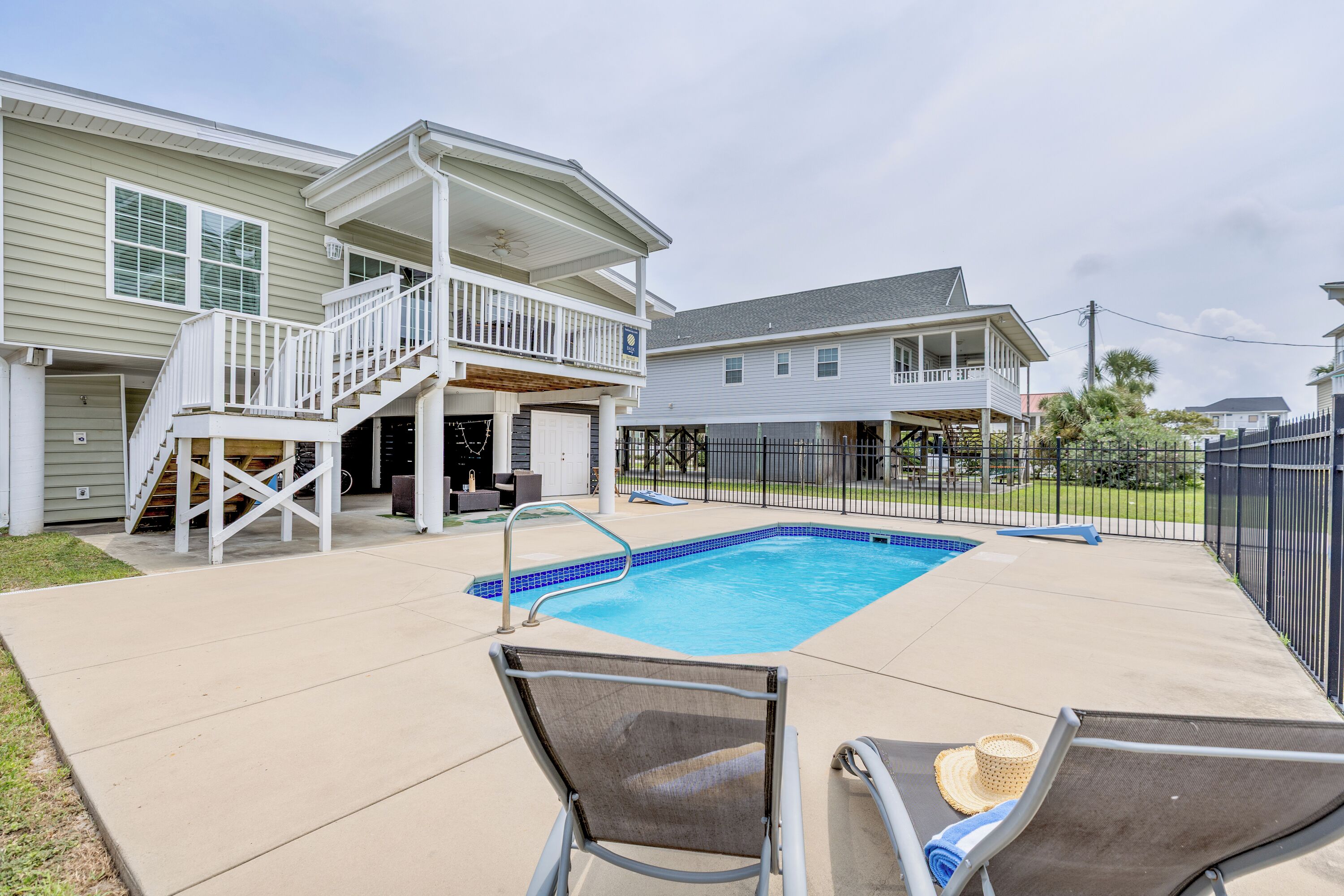 A residential backyard with a swimming pool, two lounge chairs, and a covered deck area.