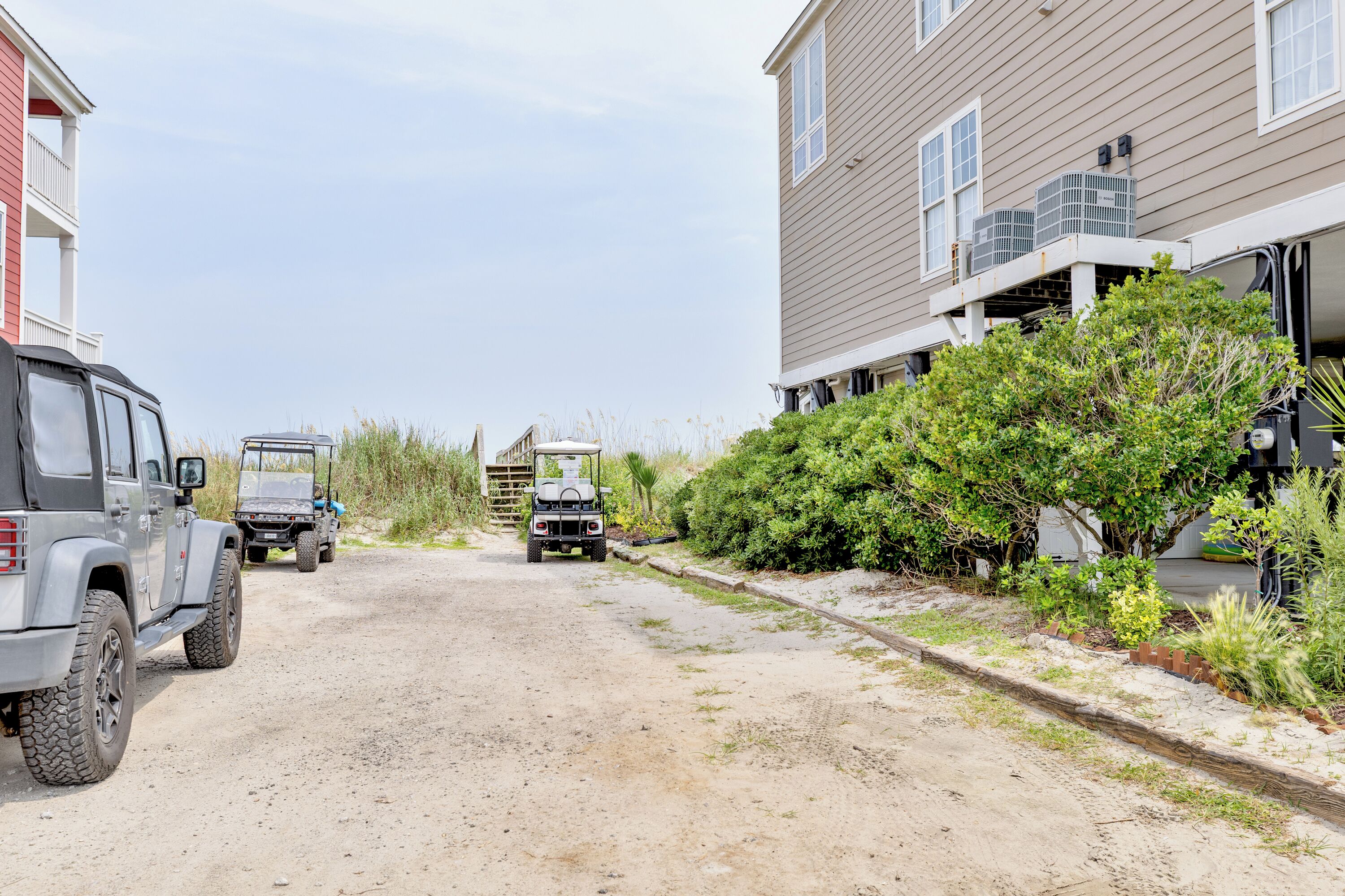 A residential street with houses, a dirt path, and parked vehicles.