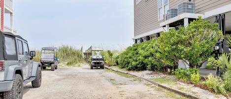 A residential street with houses, a dirt path, and parked vehicles.