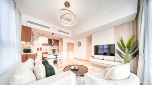Una sala moderna con un sofá, una mesa de centro y un televisor. Se observa un área de cocina al fondo, con armarios y una mesa de comedor.