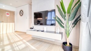Habitación de hotel moderna con televisor de pantalla plana grande, suelo de madera, planta en maceta y puerta corredera.