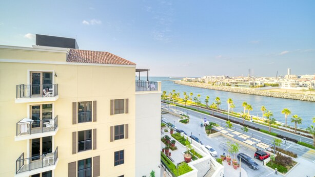 Un edificio de varios pisos con balcones, vista al mar y un estacionamiento con palmeras.