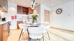 Una cocina moderna con armarios de madera, un comedor con mesa redonda y sillas blancas, y un reloj decorativo en la pared.