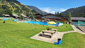 A pool area with a grassy lawn, picnic tables, and a mountain backdrop.