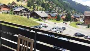 A view of a mountain village with traditional wooden houses, a road with cars, and a GO ambulance.
