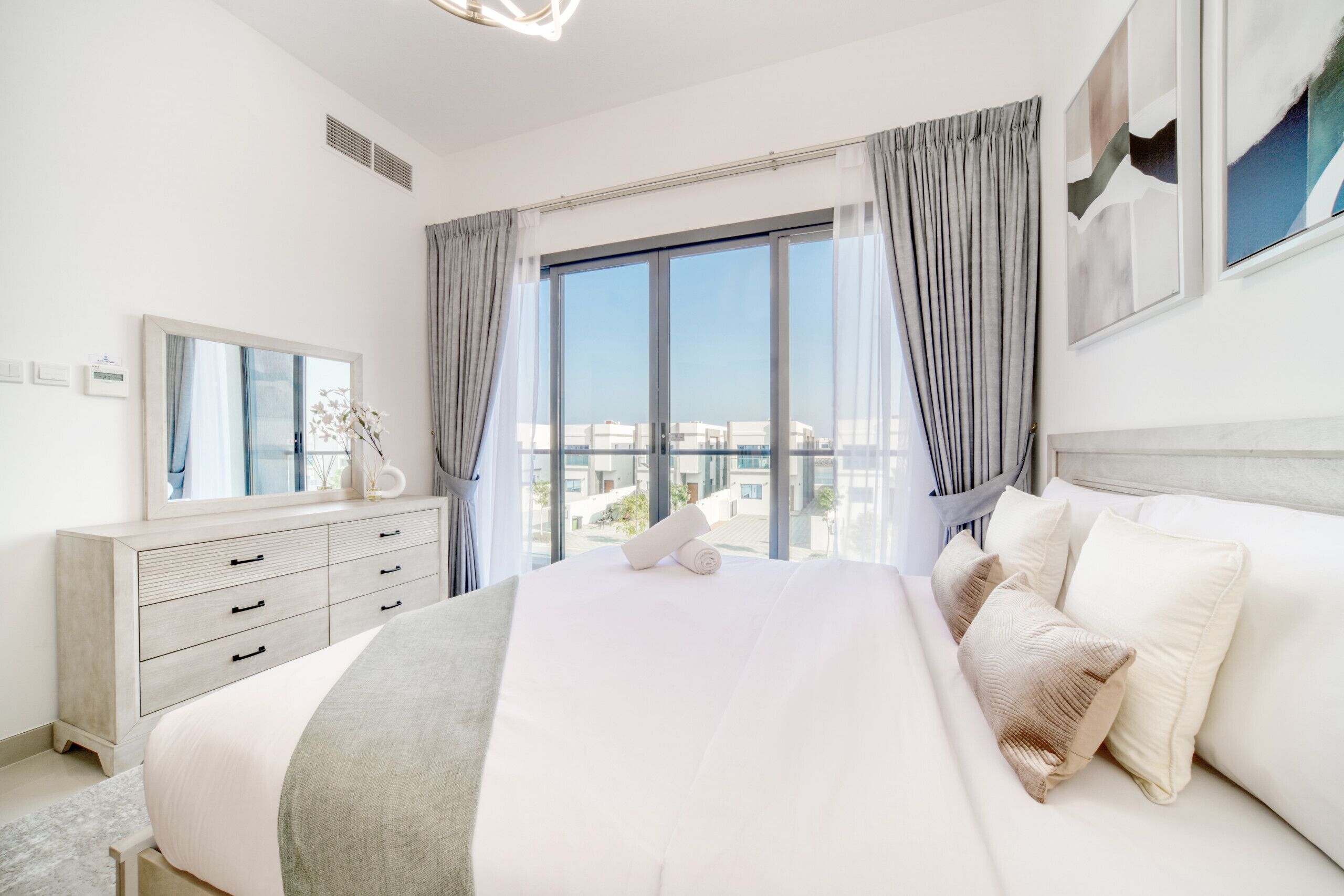 Un hotel moderno con una cama grande, un aparador, un espejo y vistas de la ciudad a través de amplias ventanas.