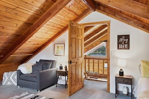 Une chambre confortable située sous les toits, avec un plafond en bois, un canapé gris, une porte en bois et une citation inspirante sur le mur.