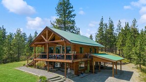 A two-story log cabin with a green roof, a covered deck, and a gravel driveway. - Lakeside Retreat in Eureka! (Eureka)