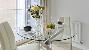Un espace repas moderne avec une table en verre, des chaises blanches, un vase rempli de fleurs et un saladier de fruits.