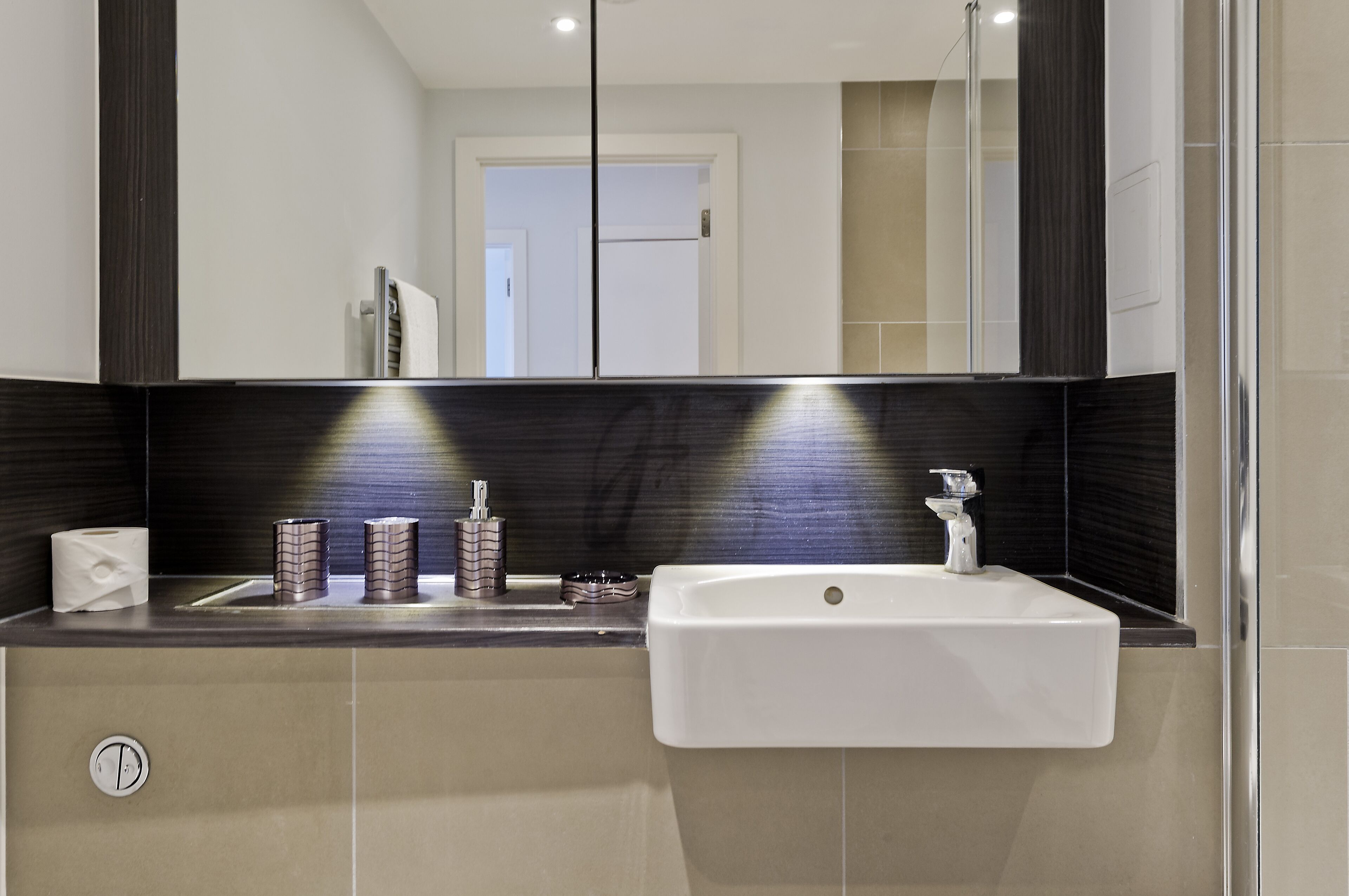A modern bathroom with a white sink, dark tiled backsplash, and a mirror above the counter.