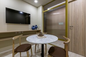 A room with a round table, two chairs, a flat-screen TV, and a sliding door.