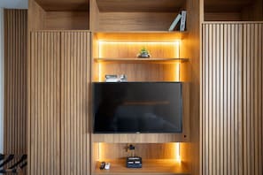 Un mueble moderno de entretenimiento con un televisor de pantalla plana, repisas iluminadas y una pequeña planta.