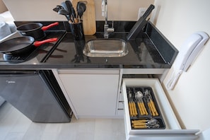 A kitchen with a black countertop, stainless steel sink, and a drawer with utensils.