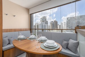 Un comedor con una mesa redonda para cuatro personas, un sofá con cojines y vistas a la ciudad a través de amplios ventanales.