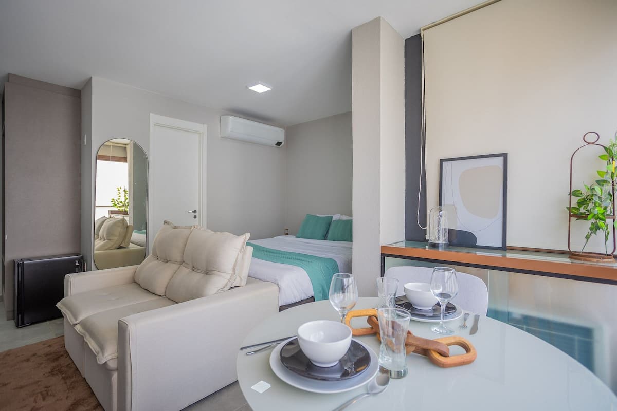 Une chambre d’hôtel moderne comprenant un lit, un canapé, une table à manger avec un saladier et des verres à vin, ainsi qu’un miroir.