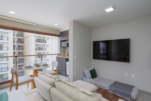 Un salon moderne avec balcon, un téléviseur à écran plat et un coin repas comprenant une table et des chaises.