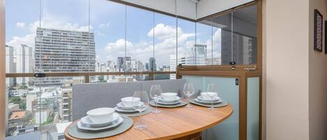Un comedor moderno con una mesa de madera dispuesta para cuatro, ventanas amplias con vista a la ciudad y un portazo corredizo que da a un balcón.