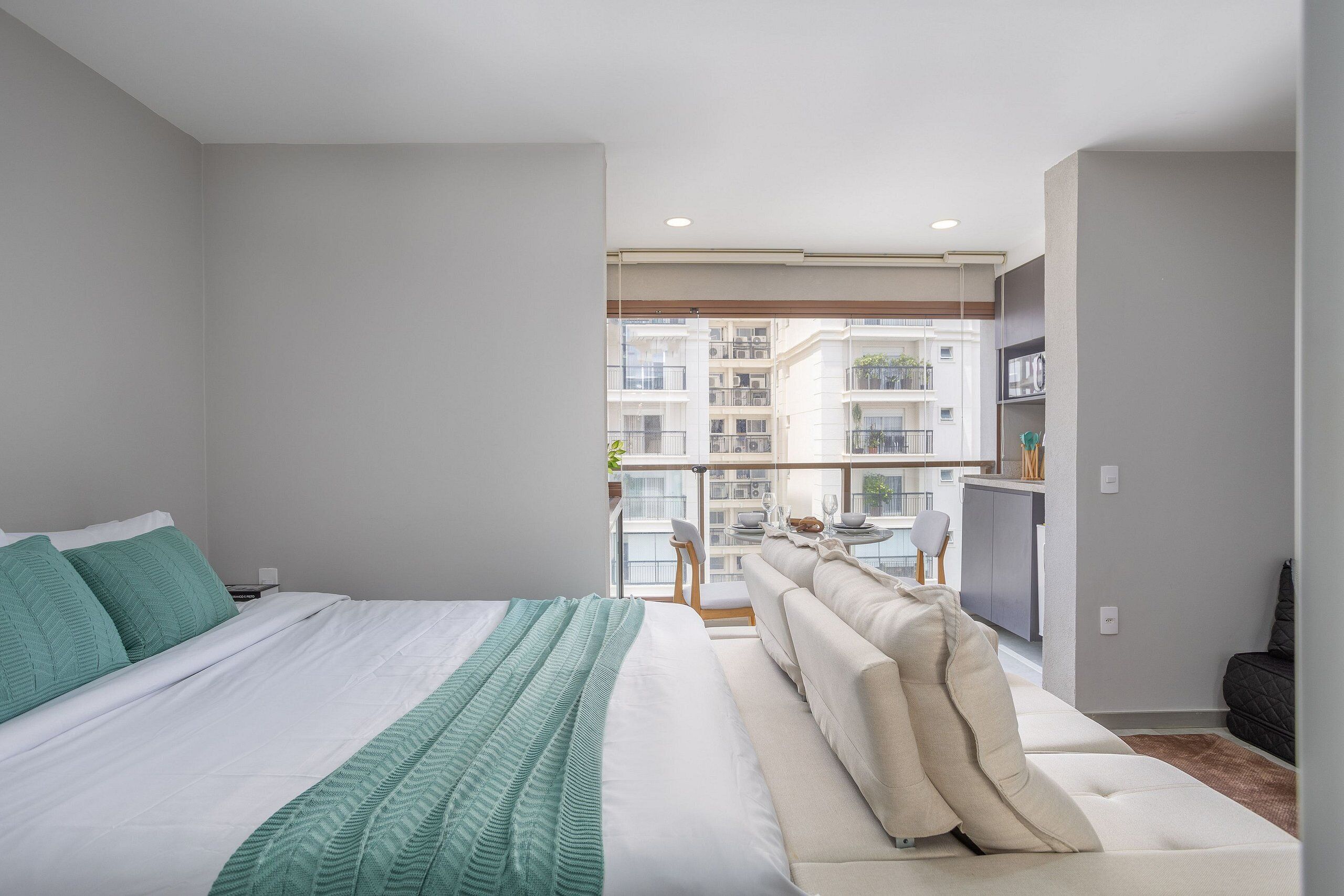 Quarto moderno com cama grande, sofá e varanda com vista para outros edifícios.