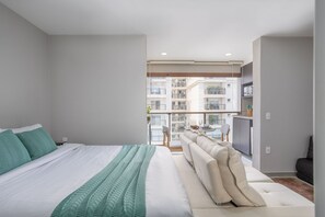 Une chambre moderne avec un grand lit, un canapé et un balcon offrant une vue sur les autres immeubles.