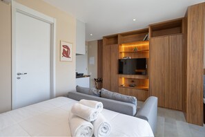 Une chambre d’hôtel moderne équipée d’un lit, d’un canapé, d’une télévision et d’étagères en bois.