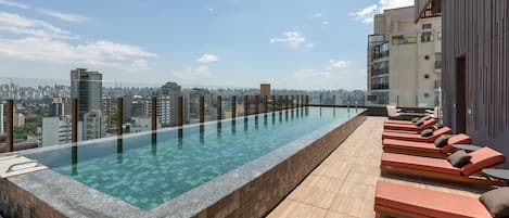 A rooftop infinity pool with lounge chairs and a city view.