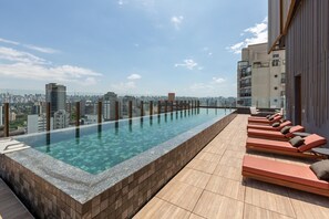 A rooftop infinity pool with lounge chairs and a city view.