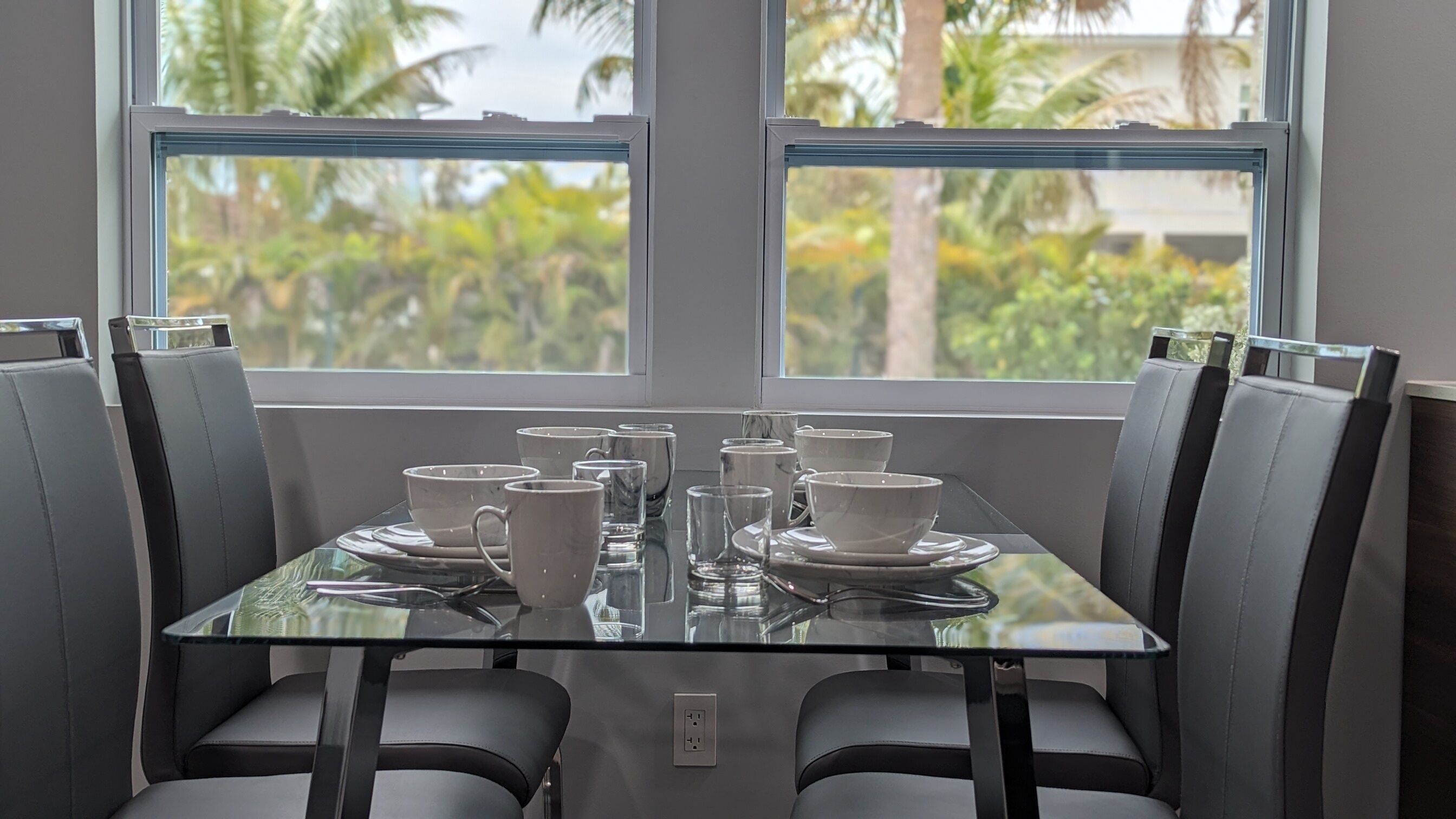 A dining table with chairs, a glass top, and white tableware.