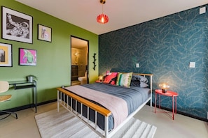 Ein Schlafzimmer mit einem Bett, einem Nachttisch, einer roten Lampe und gerahmten Kunstwerken an der Wand.