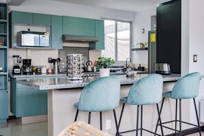 A modern kitchen with teal cabinets, a granite countertop, and three bar stools. - Private Terrace Escape in the Heart of Roma Norte (Ciudad de México)