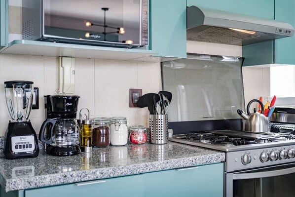 A kitchen with a gas stove, a blender, a coffee maker, and various jars on the counter.