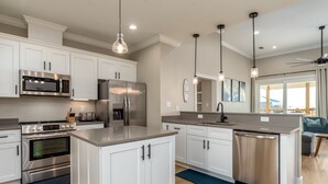 A modern kitchen with white cabinetry, stainless steel appliances, and pendant lighting.