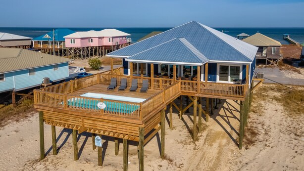 A beach house with a pool, wooden deck, and ocean view.