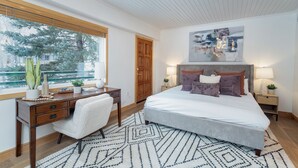 Una camera da letto con un letto grande, una scrivania, una sedia, una finestra vista alberi e un quadro appeso al muro.