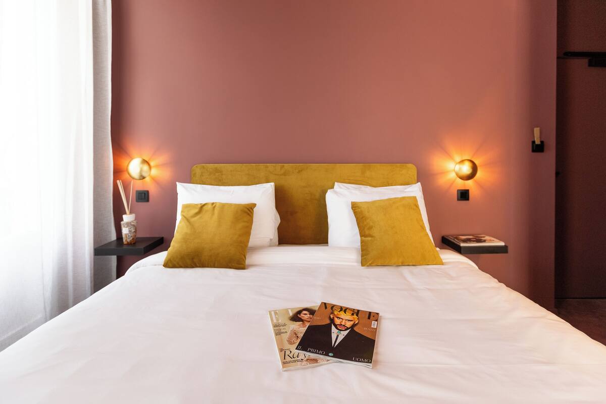 A hotel room with a bed, two bedside tables, and two wall-mounted lamps.