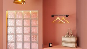 A pink room with a hanging light, a white cabinet with a bowl of fruit, and a white hanging rack. - The Mila Brussels (Brussels)